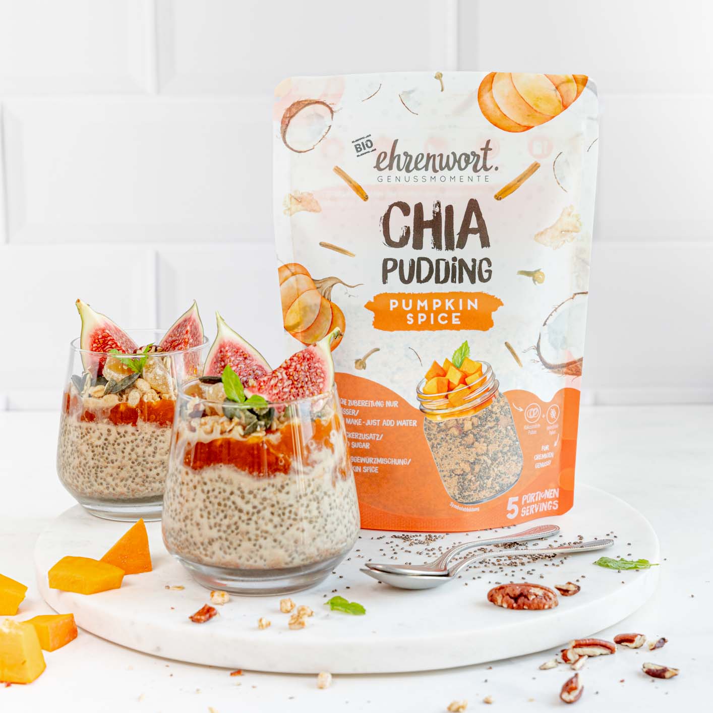 ehrenwort BIO Pumpkin Spice Chia Pudding Verpackung neben zubereiteter Portion in einem weißen Raum auf Präsentierteller neben Kürbis stücken und Samen